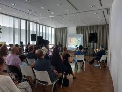 Viele Zuschauer schauen einen Film auf einer Leinwand. Rechts der Leindwand sitzen Musiker, die zu dem Film spielen.