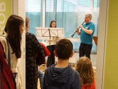 Mehrere Kinder hören einem Musikschullehrer und einer Schülerin beim Spielen zu.