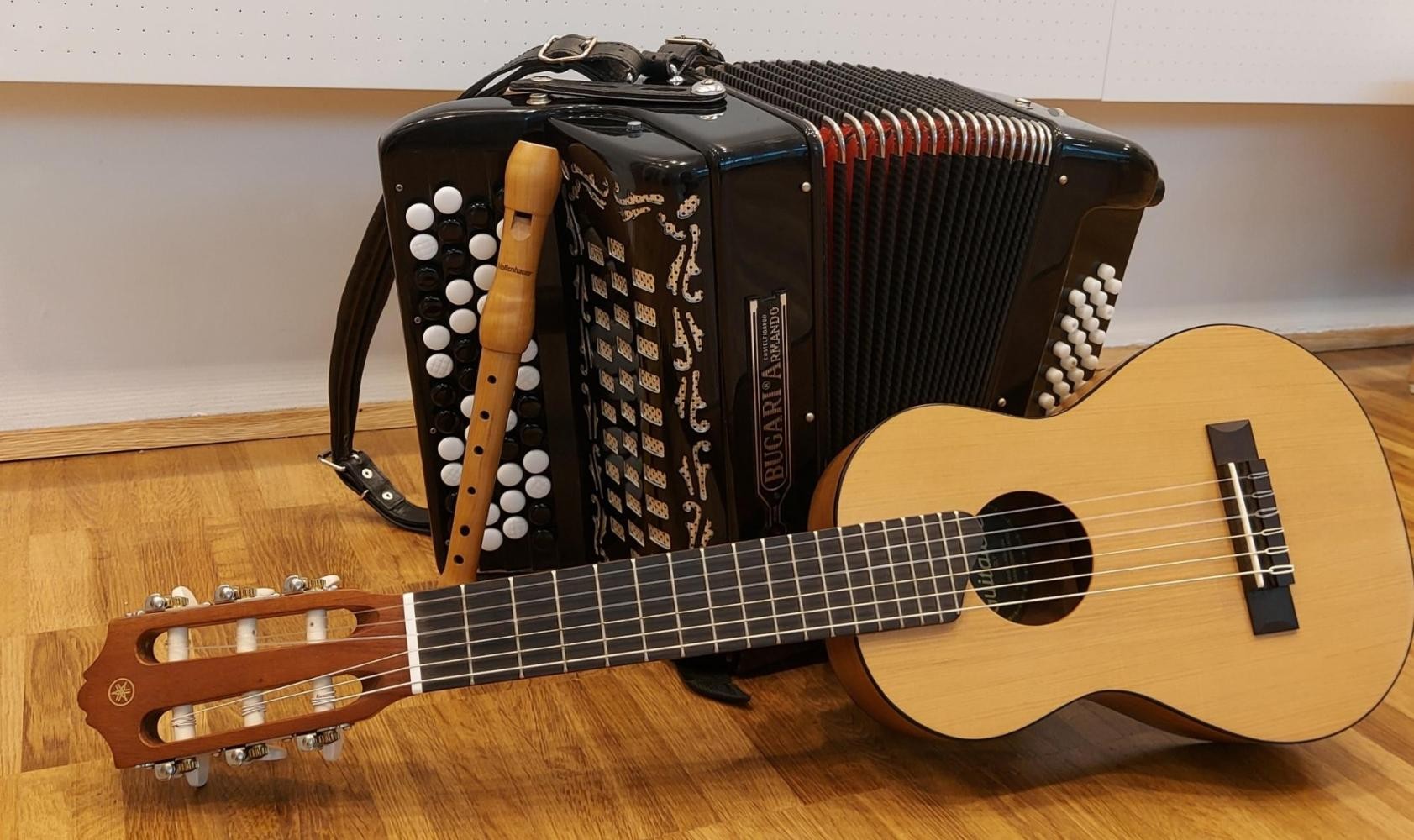 Eine Gitarre und eine Blockflöte lehnen an einem Akkordeon.