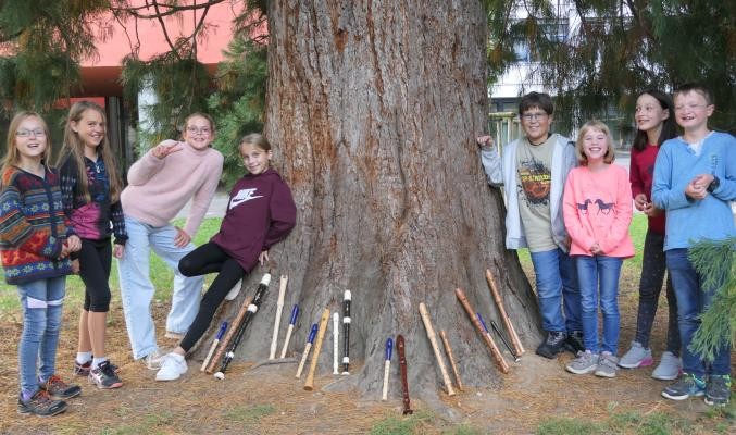 Die Kinder, die im Ensemble "Easy going" spielen, stehen neben einem großen Baum, an den sie ihre Flöten gelehnt haben