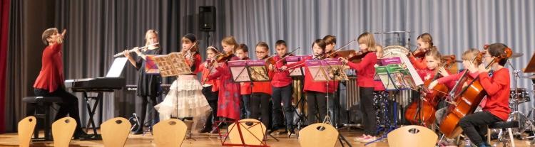 Auf der Bühne sind Musikschüler und die Leiterin des Kinderkammerorchesters.