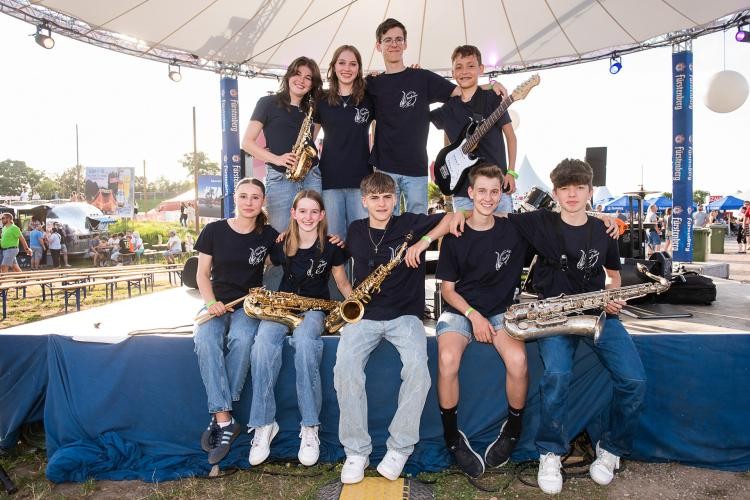 Die "SaxoGrooves" Kindermusik Gruppe sitzt gemeinsam auf einer Bühne.
