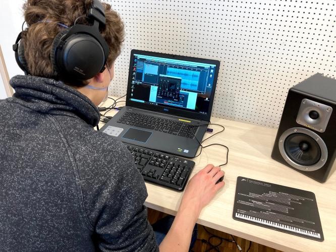 Eine Person sitzt an einem Computer. Sie trägt Kopfhörer und arbeitet.