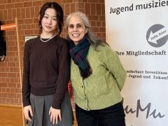 Die Schülerin Elena Chen steht mit ihrer Klavierlehrerin Patricia Germano vor dem Banner von Jugend Musiziert.