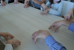 Kinder und ein Musikschullehrer sitzen an einem Tisch. Man sieht nur Hände und Arme der Personen.