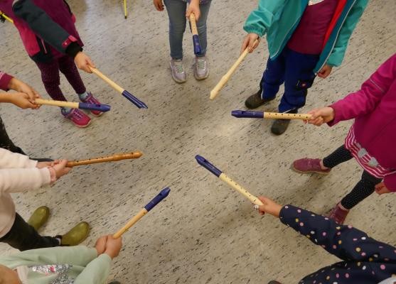 Kinder stehen in einem Kreis und halten ihre Blockflöten in die Mitte.
