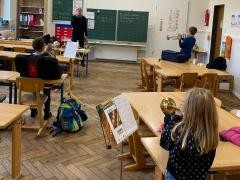 Ein Kind spielt Trompete in einem Klassenzimmer. Im Hintergrund sind noch andere musizierende Kinder zu erkennen.