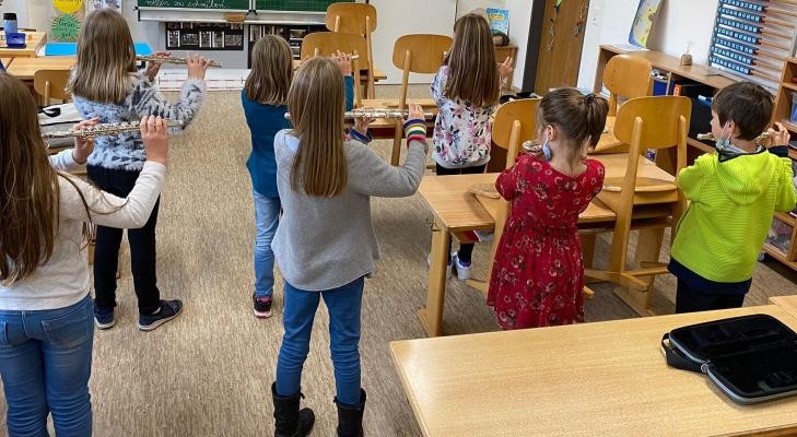 Mehere Kinder stehen in einem Klassenzimmer und spielen Querflöte.