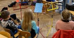Mehrere Kinder sitzen vor einem Notenständer und musizieren.