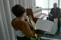 Ein Kind mit Horn steht vor seinem Musikschullehrer und speilt.