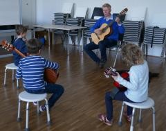 Gitarrenunterricht in der Musikschule: drei Kinder sitzen mit Stefan Goeritz in einem Kreis.