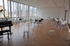 Musikzimmer mit vielen Stühlen, Notenständer und einem Piano.