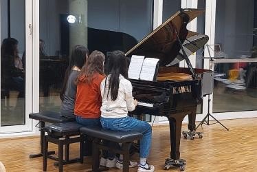 Drei Schülerinnen sitzen und spielen gemeinsam am Piano.