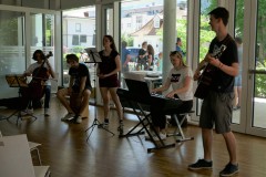 Ein Esemble aus jungen Musikern die verschiedene Instrumente spielen darunter ein Cajón, Cello, Gitarre, Piano.,  