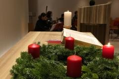 Ein Adventskranz mit einer angezündeten Kerze und der aufgeschlagenen Bibel.