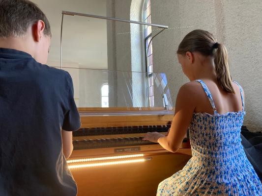 Eine Klavierschülerin übt auf der Orgel, während der Orgellehrer zusieht und daneben sitzt.