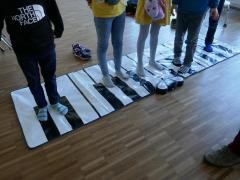 Kinder stehen auf einer großen Klaviertastatur.