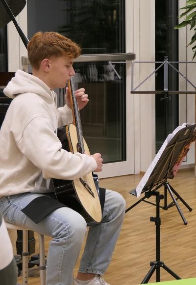 Ein junger Mann der auf einer akkustischen Gitarre spielt.