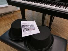 Tastatur des Flügels und 2 Zylinder-Hüte mit Programm auf der Klavierbank.