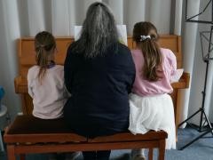 Klavierlehrerin sitzt mit zwei kleinen Schülerinnen zusammen am Klavier.