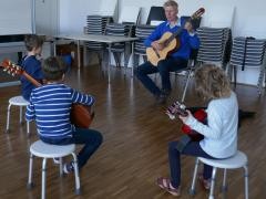 Herr Goeritz unterrichtet drei junge Schüler*innen mit Gitarren.