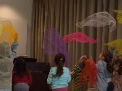 Kinder werfen bunte Rhythmustücher in die Luft und fangen sie wieder.