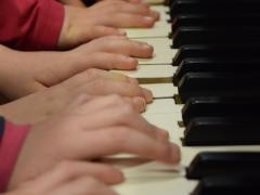 Viele Kinderhände spielen zusammen auf einer Klaviertastatur.